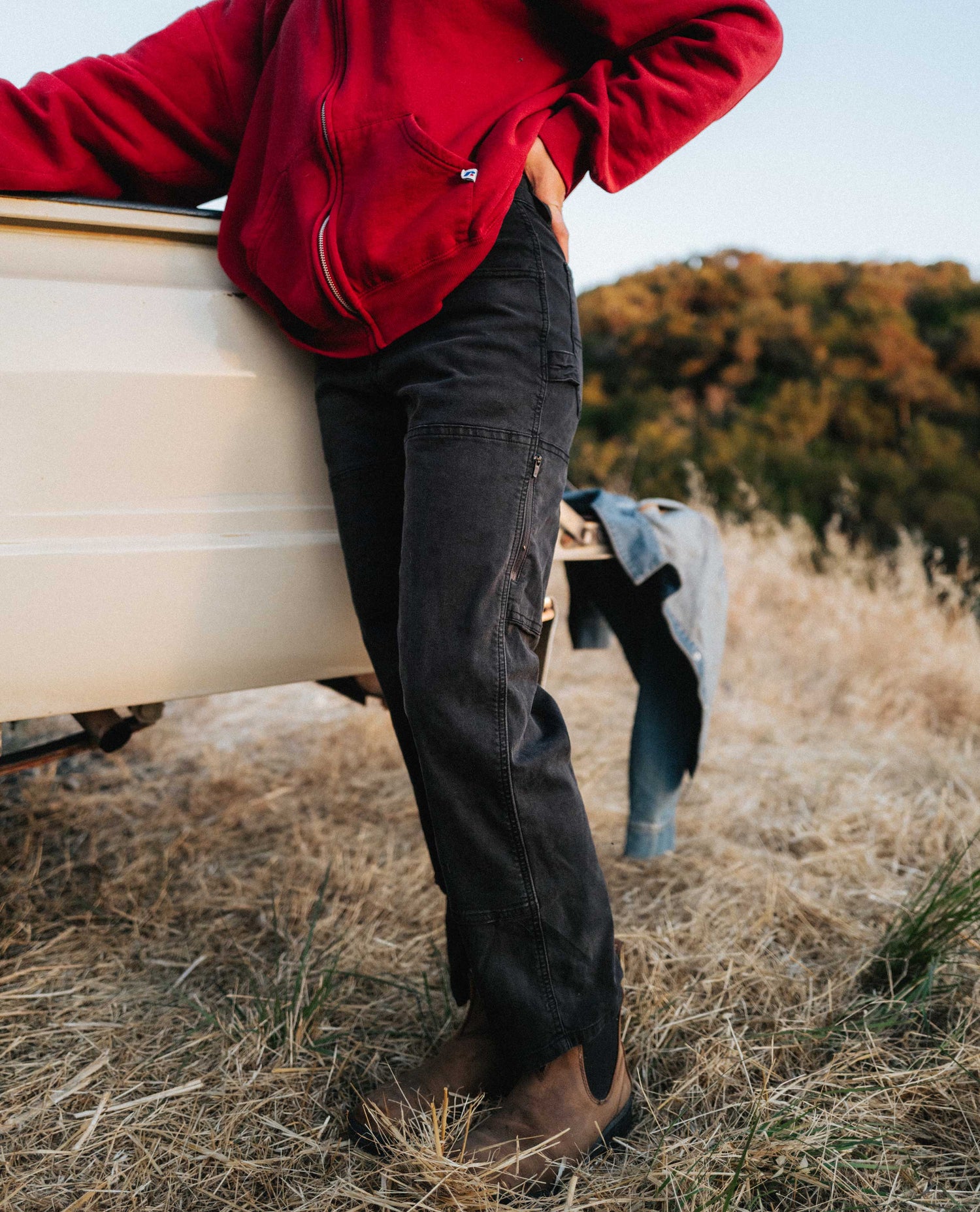Girl wearing black utility pants with red top next to a pickup truck