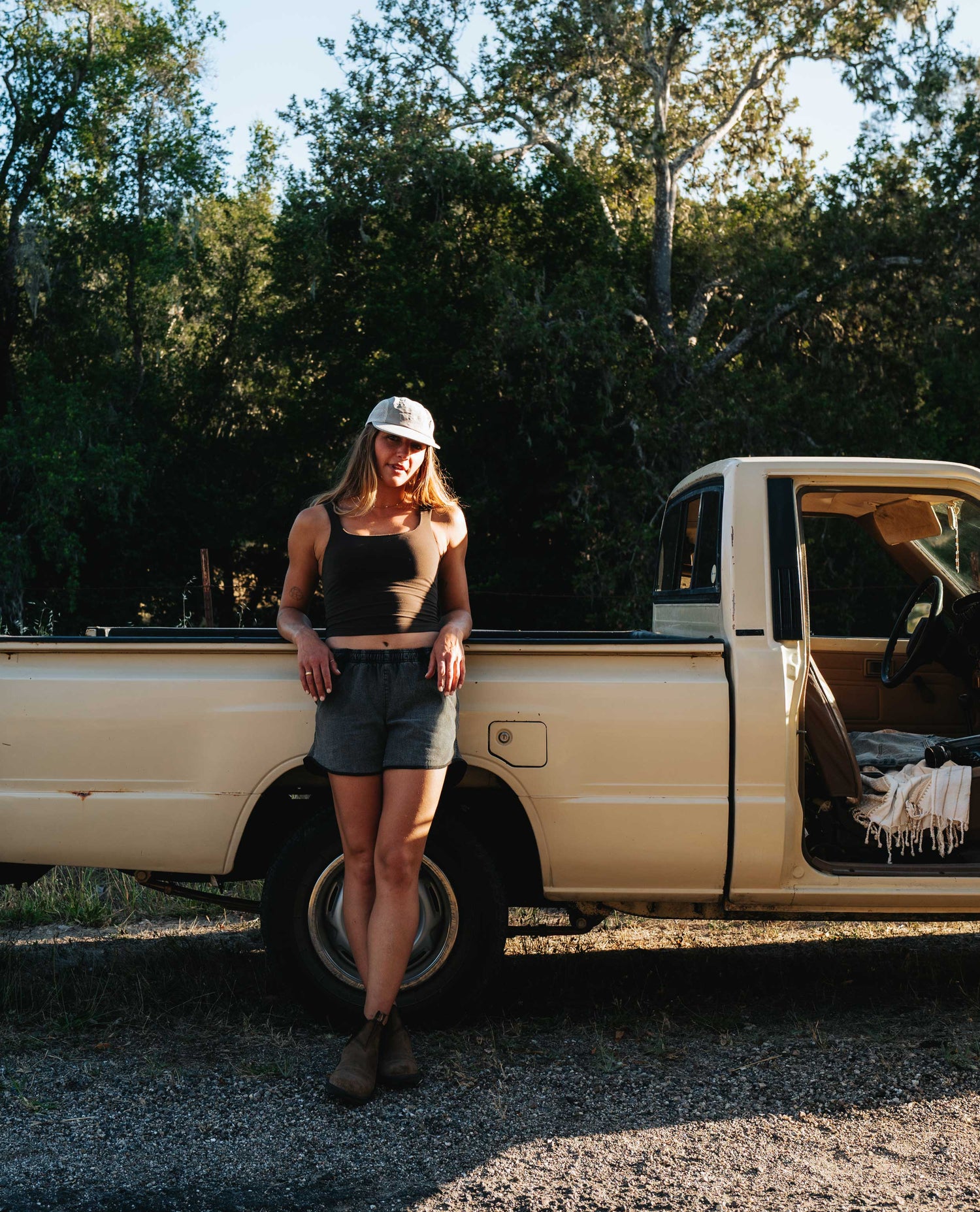 Girl leaning against a pickup truck with gray running shorts and blundstones