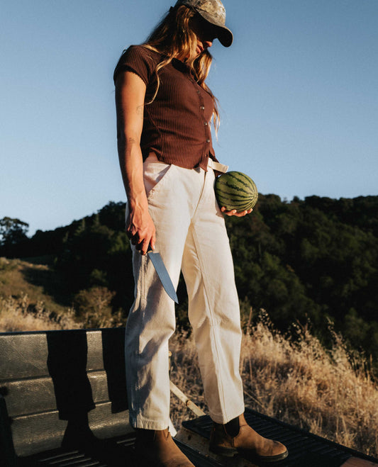Girl wearing white flux pants holding a watermelon and a knife