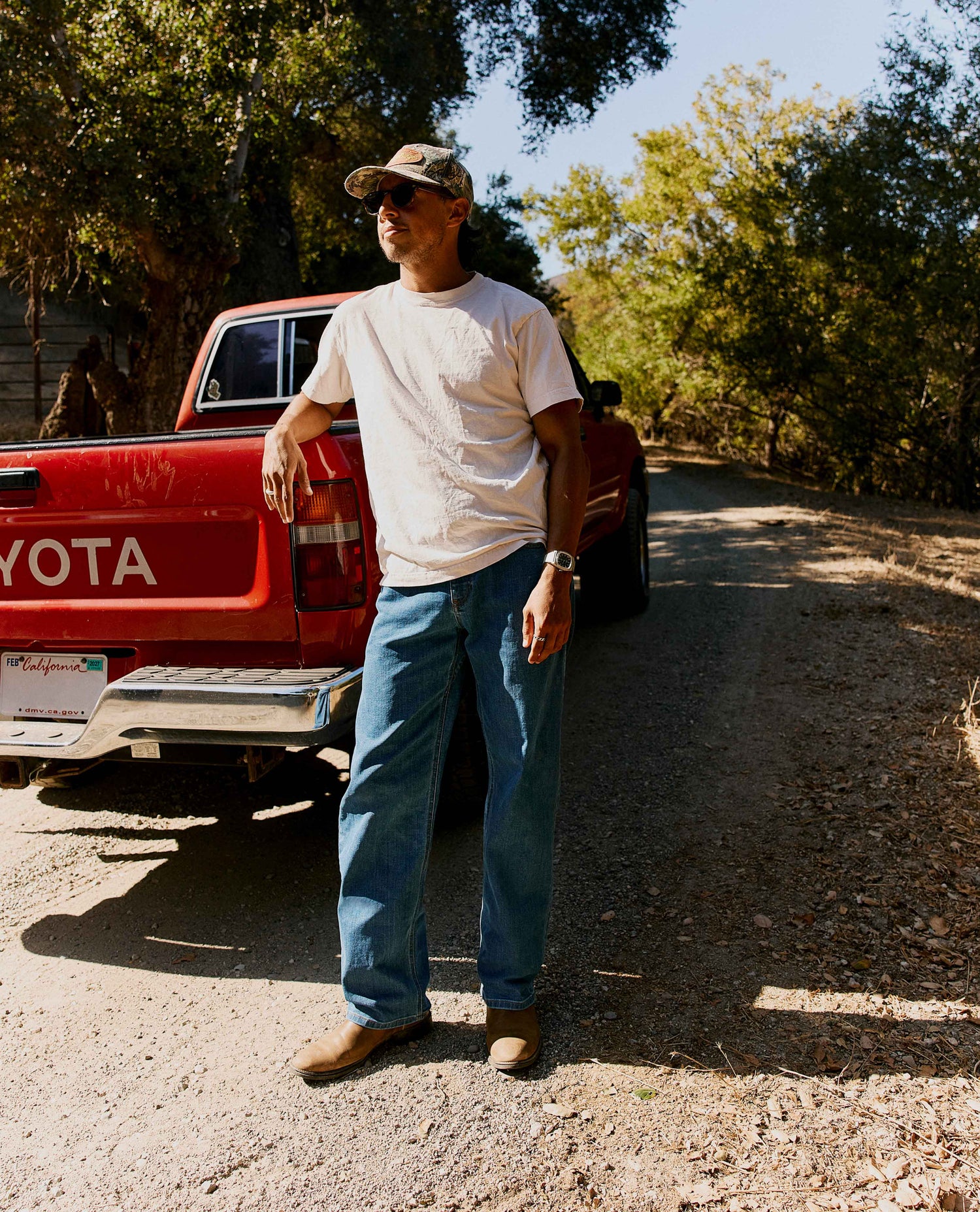 Man standing next to red truck, wearing a white shirt and blue jeans.