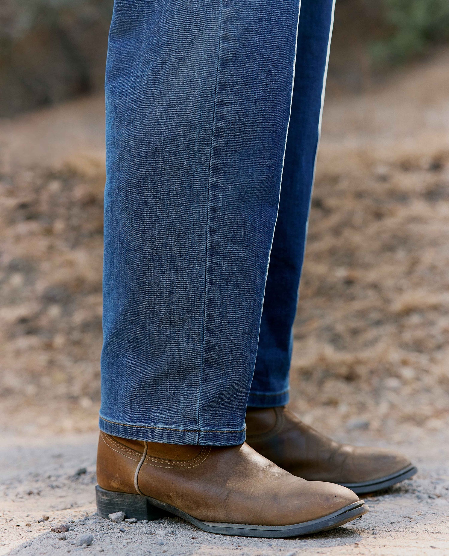 Close up of blue jeans, with cowboy boots, in front of dusty background.