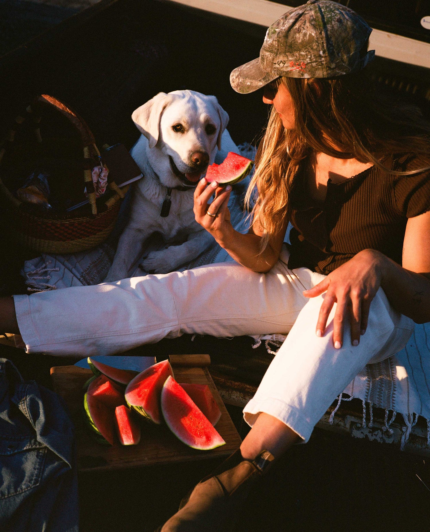 Girl eating watermelon with her dog in the back of a pickup truck