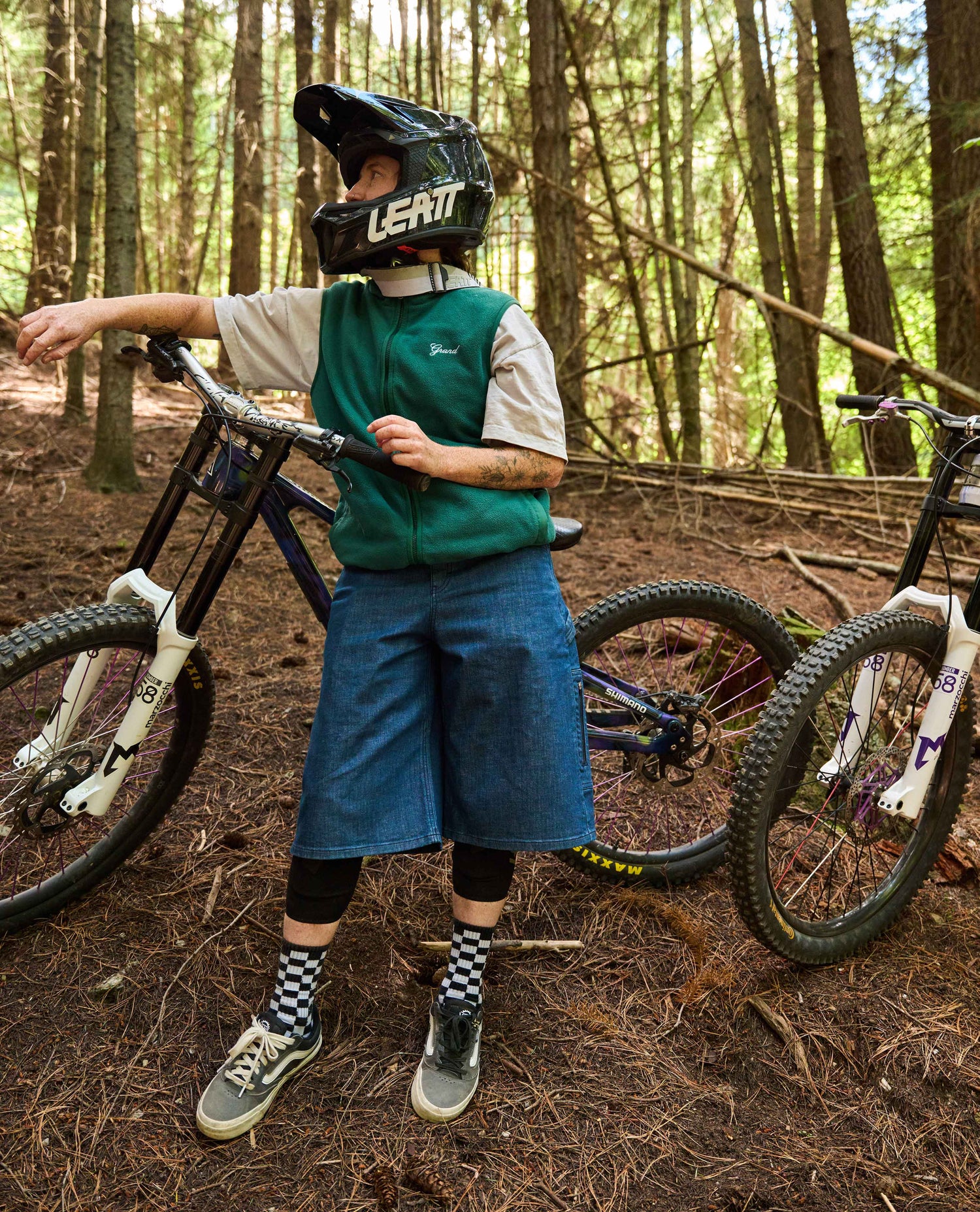Person with a bicycle in a forest setting wearing a helmet and green vest.