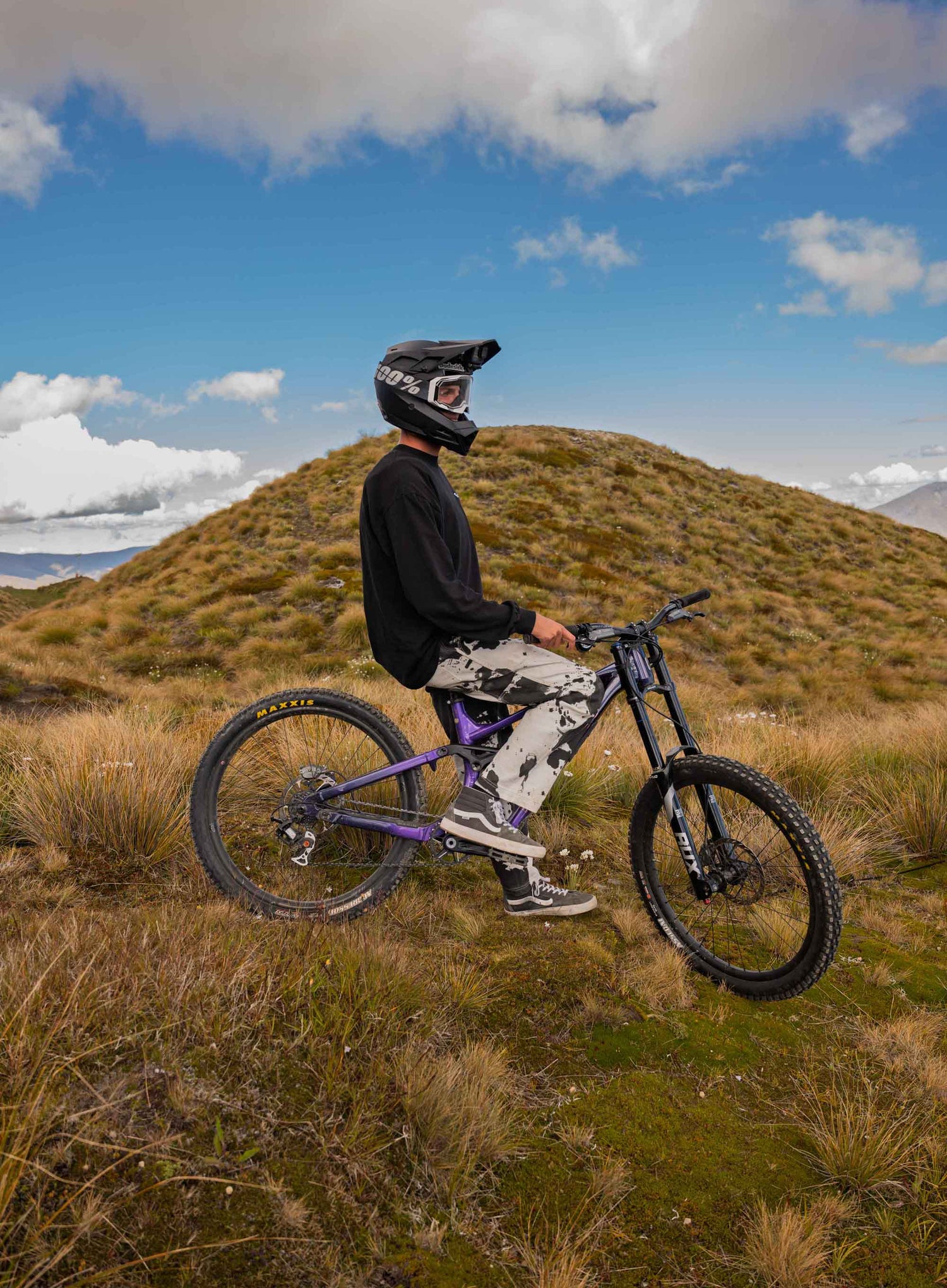 Person on a mountain bike in a scenic outdoor setting with grassy hills and blue sky.