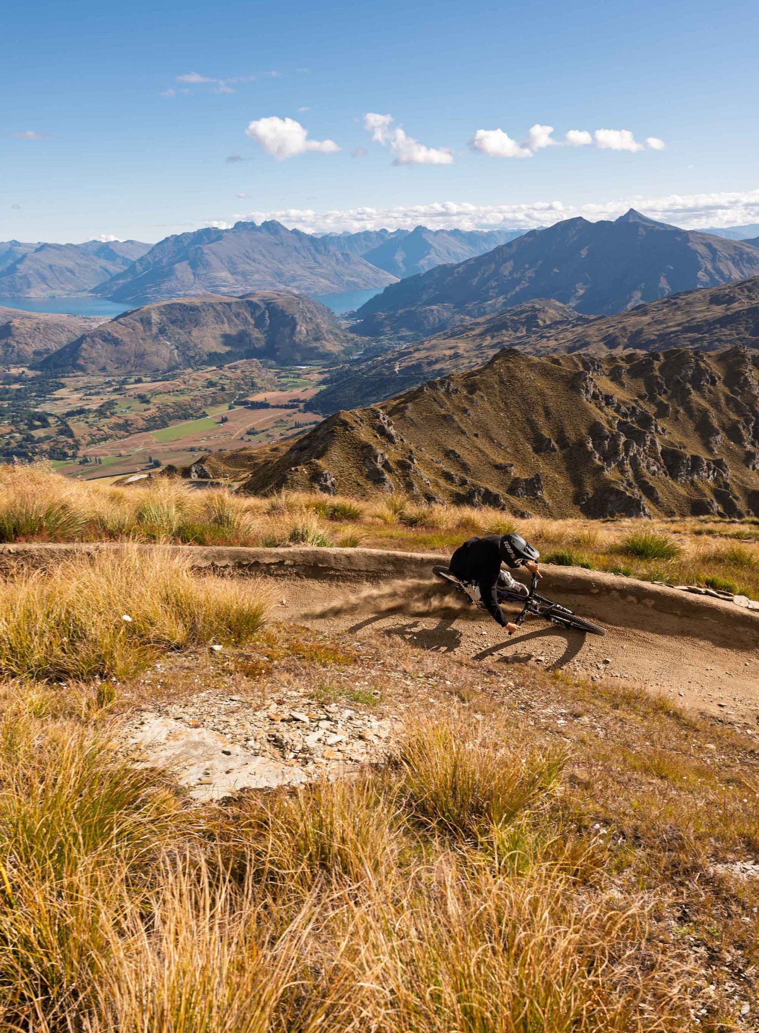 Person with a bicycle on a mountain path with scenic mountains and lake in the background