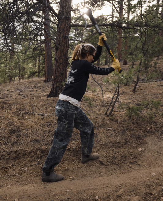Woman wearing pant with leaf camouflage pattern swinging an axe. 