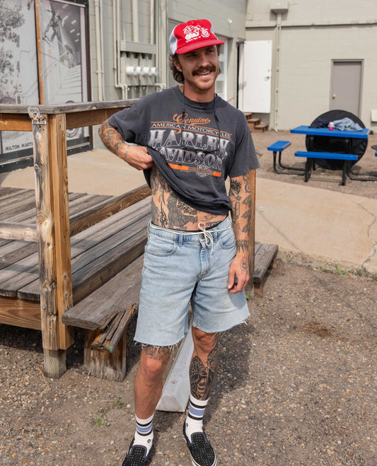 Man wearing a Harley Davidson t-shirt and denim shorts standing outdoors.