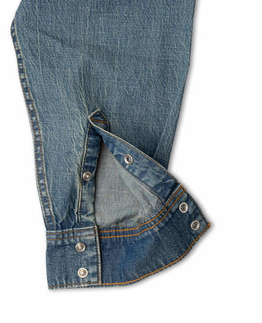 Close-up of a blue denim garment, showing the fabric texture, stitching, and silver metal snap buttons on a white background.