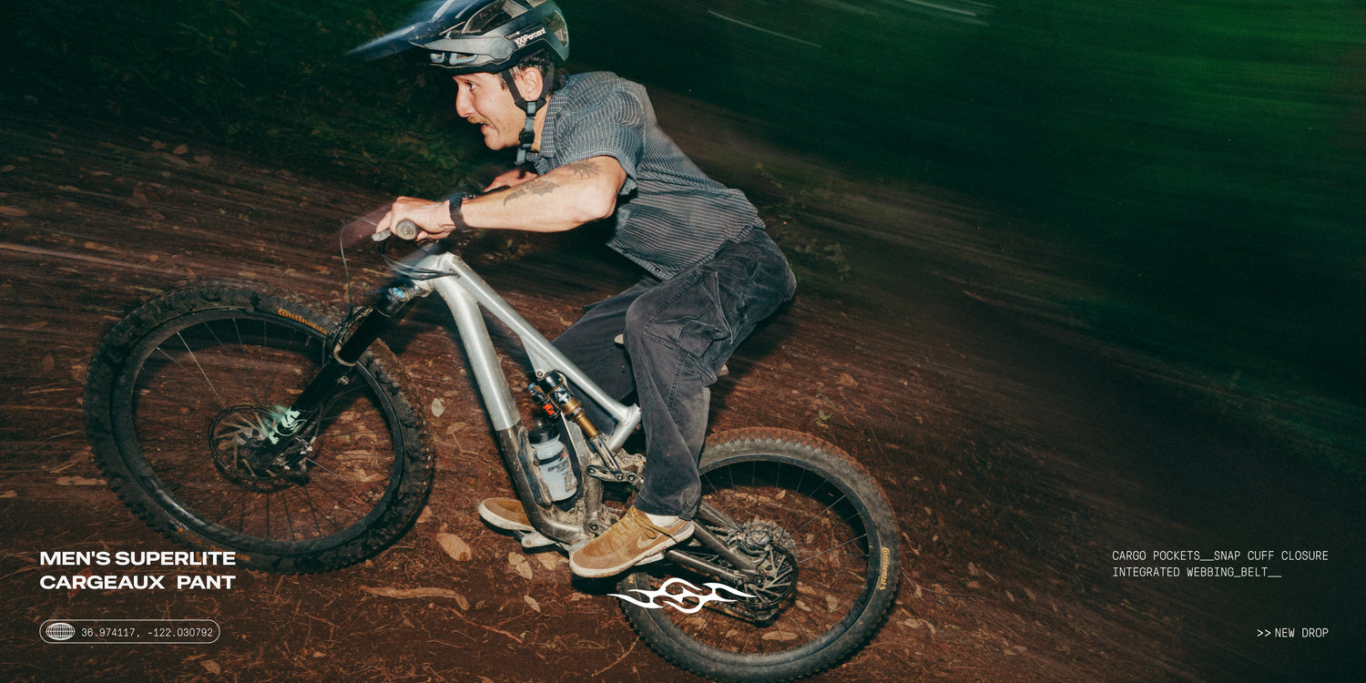 A man wearing a black helmet and a dark gray mountain bike riding on a dirt trail at night, with text overlays for 'Men's Superlite Cargueux Pant' by Mizz Rop.