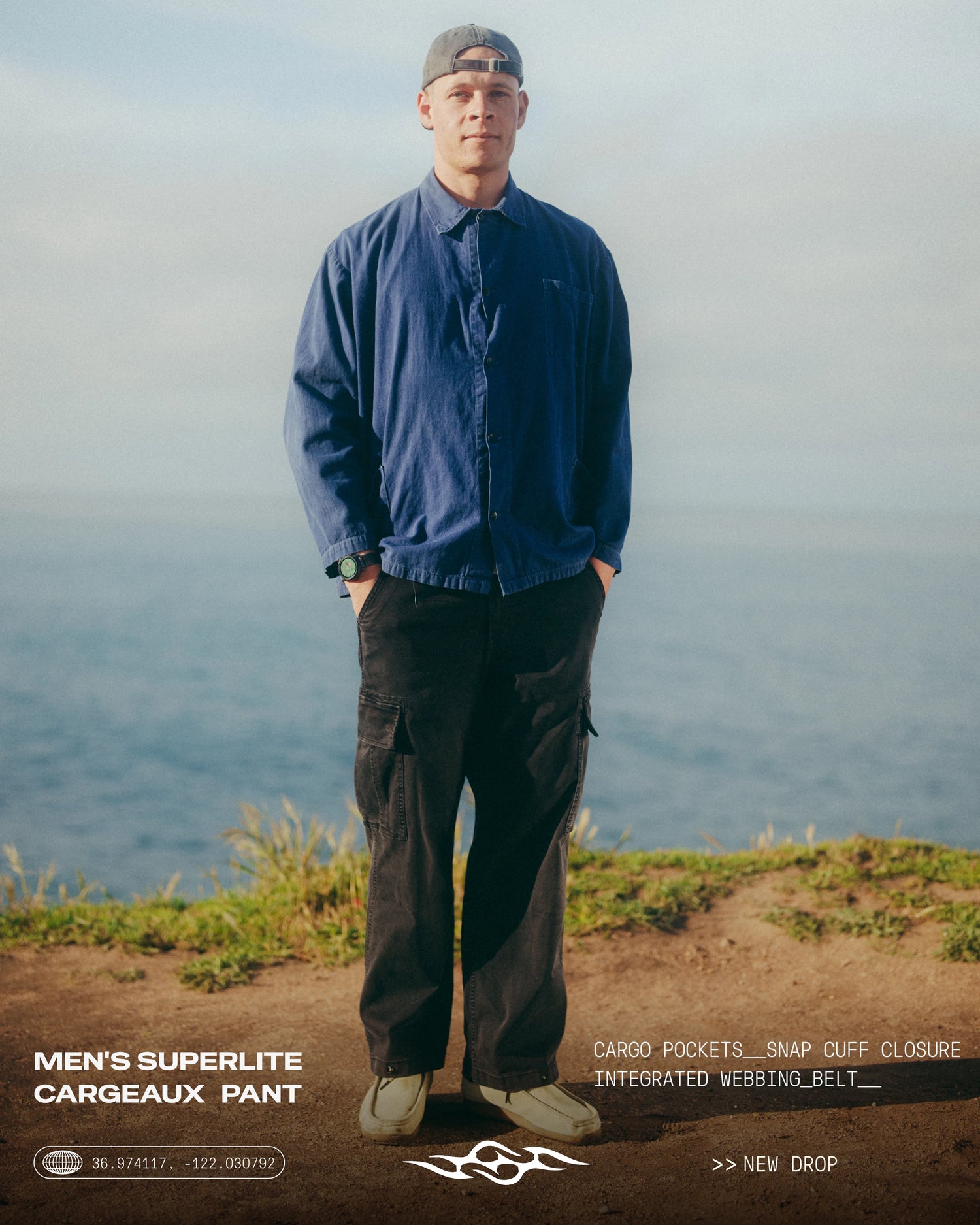 A man stands on a grassy cliff overlooking the ocean, wearing a blue button-up overshirt, dark cargo pants, and a gray cap. Text overlays at the bottom mention the Men's Superlii Cargeaux Pant.
