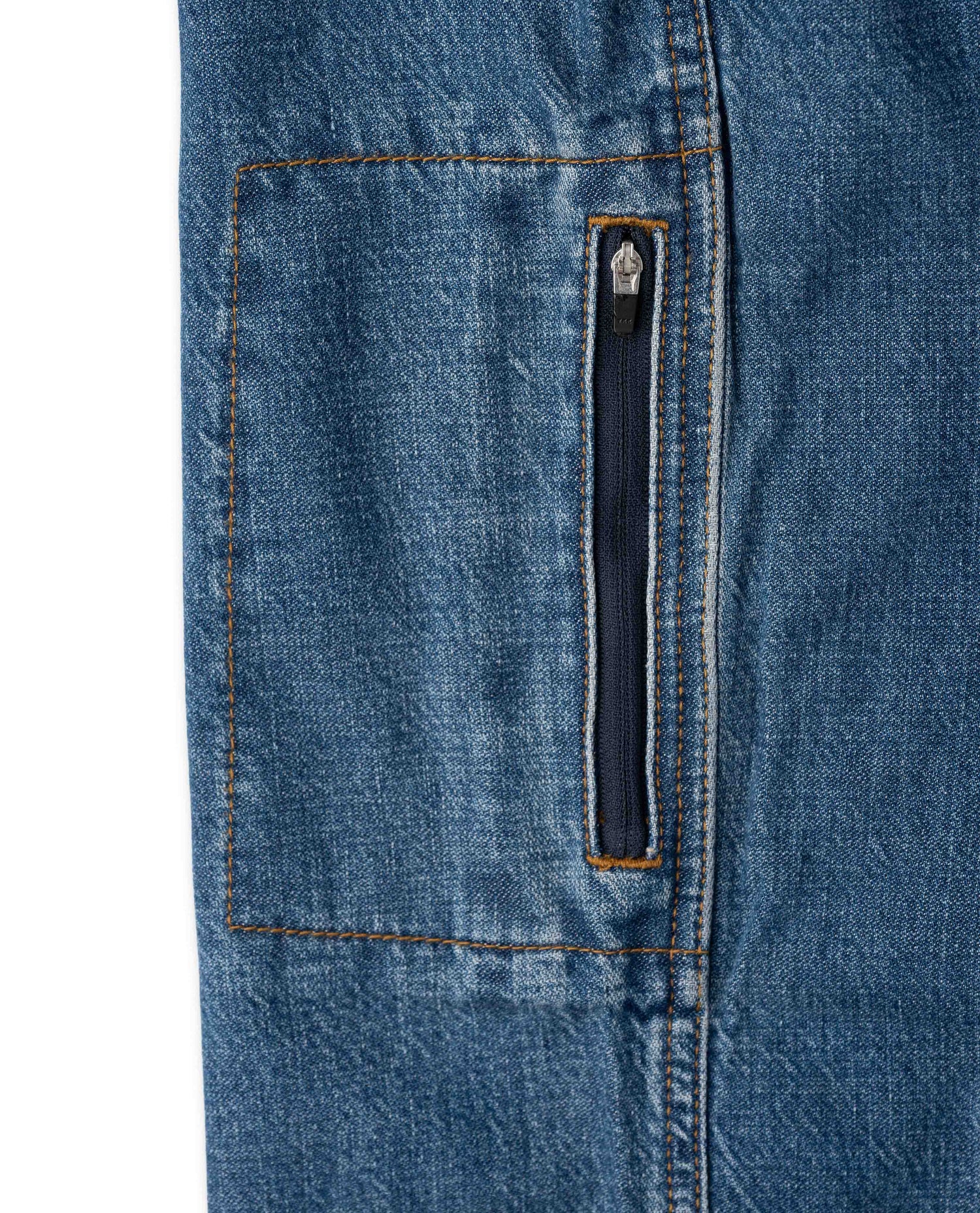 Close-up of a blue denim jacket showing a front pocket with orange contrast stitching and a vertical zippered pocket.