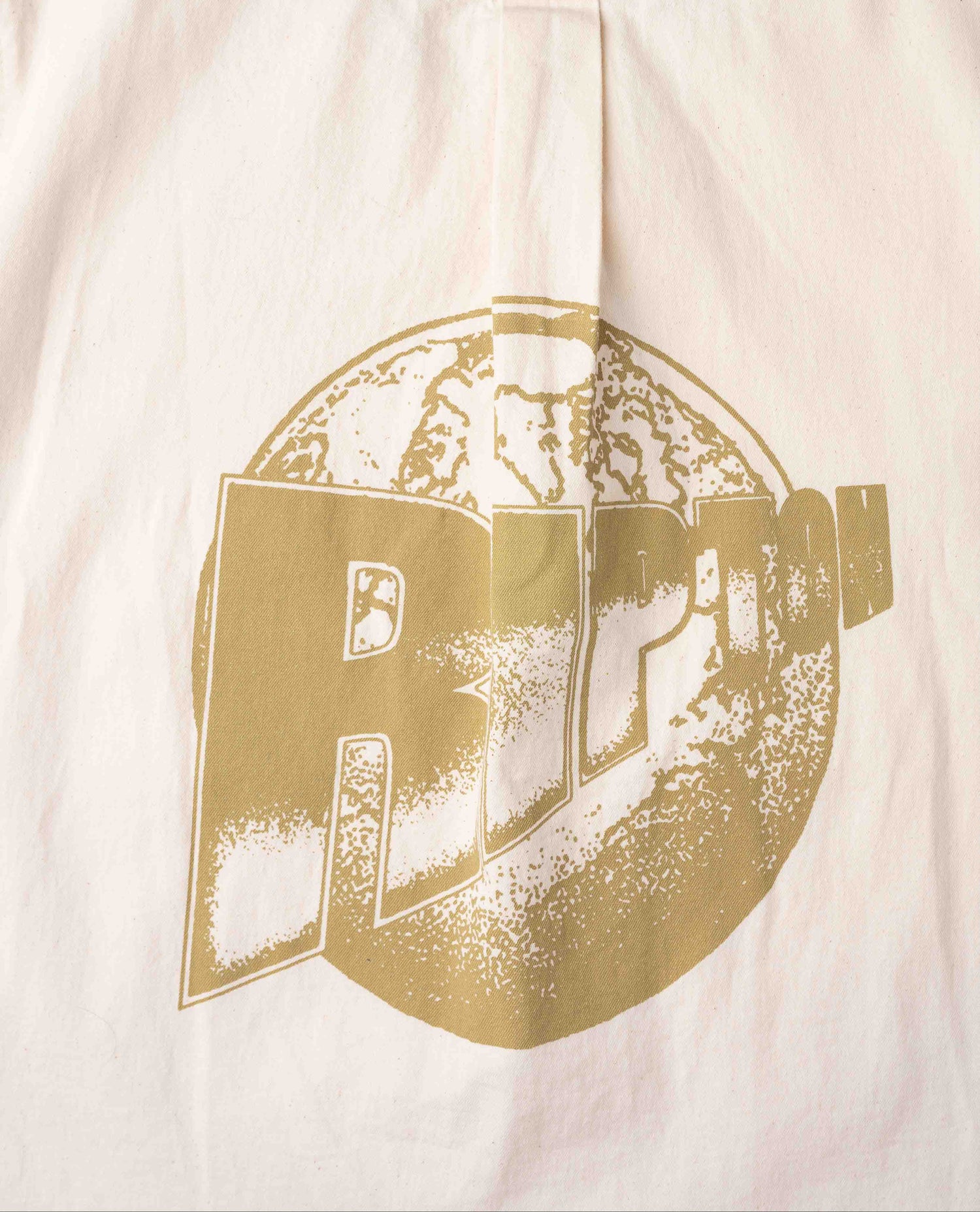Close up of gold Ripton logo on white shirt.