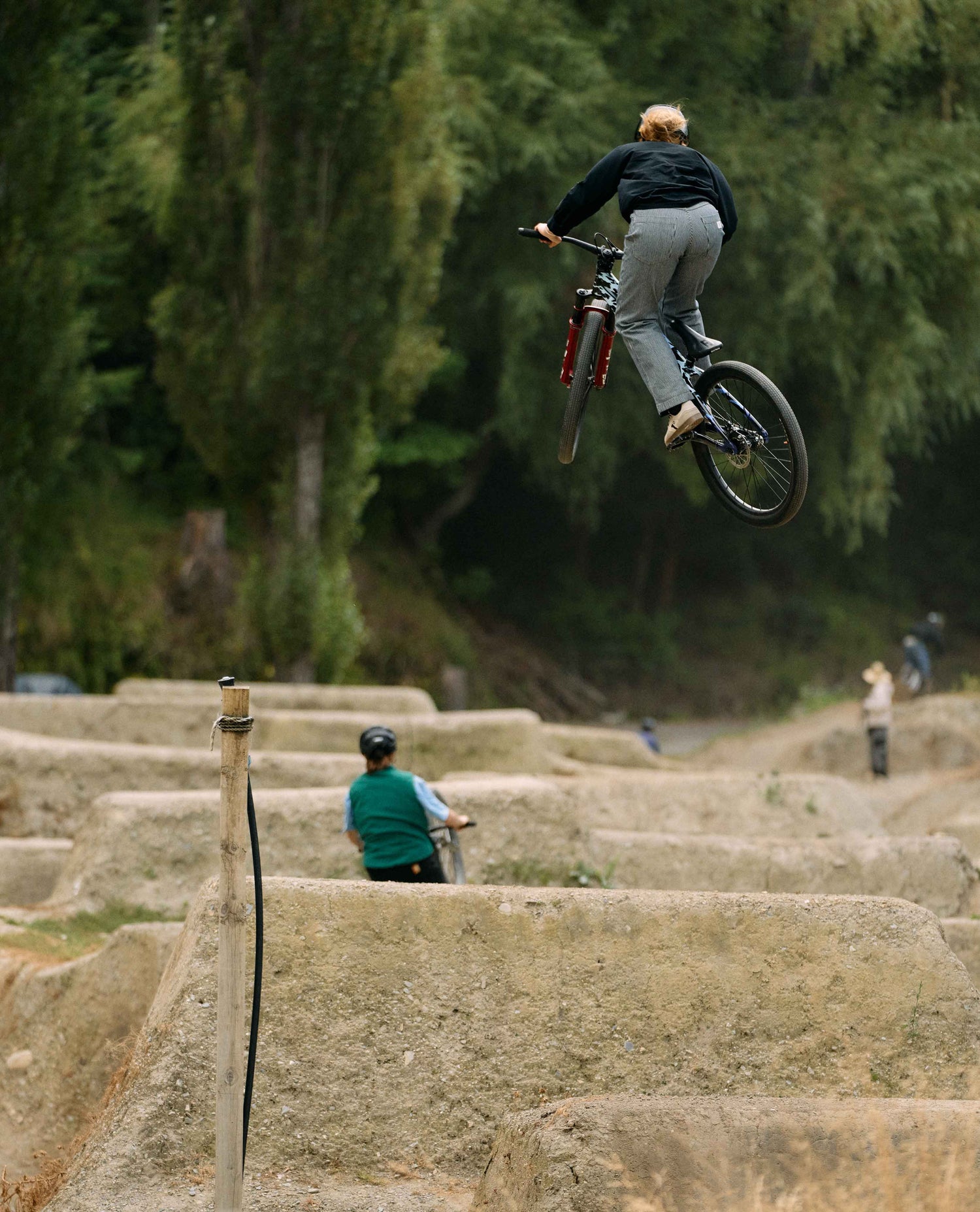 Person on a bicycle performing a jump in an outdoor setting with trees in the background
